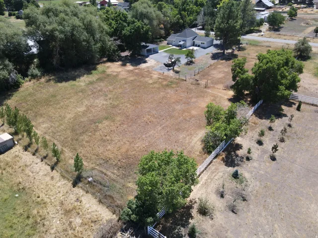 Expansive lot with a single-story residence and detached garage, featuring mature perimeter trees, a white picket fence, and additional smaller trees