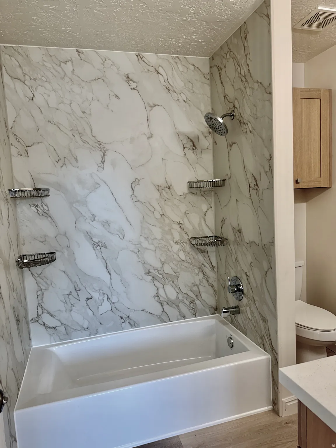 Bathtub and shower combination featuring a white tub, chrome showerhead, and wall-mounted shower caddy