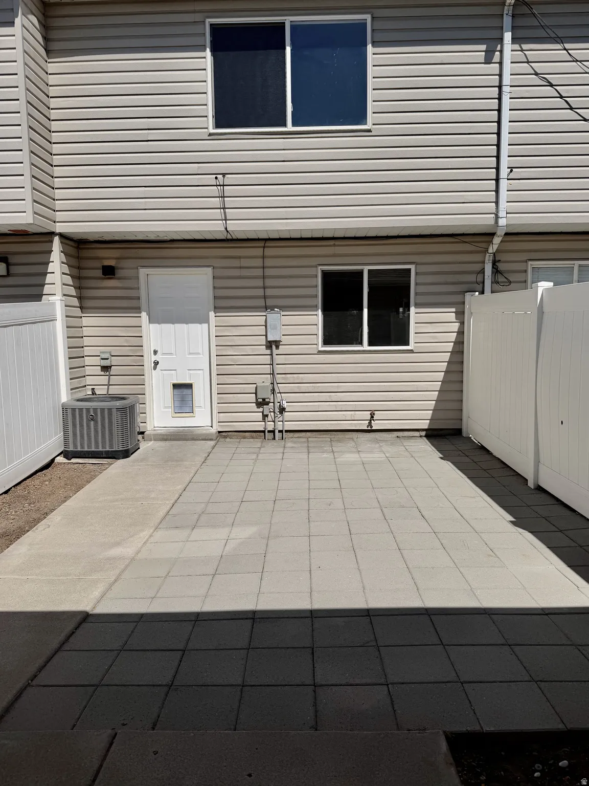 Paved patio area featuring light gray pavers, concrete walkway, and vinyl privacy fencing