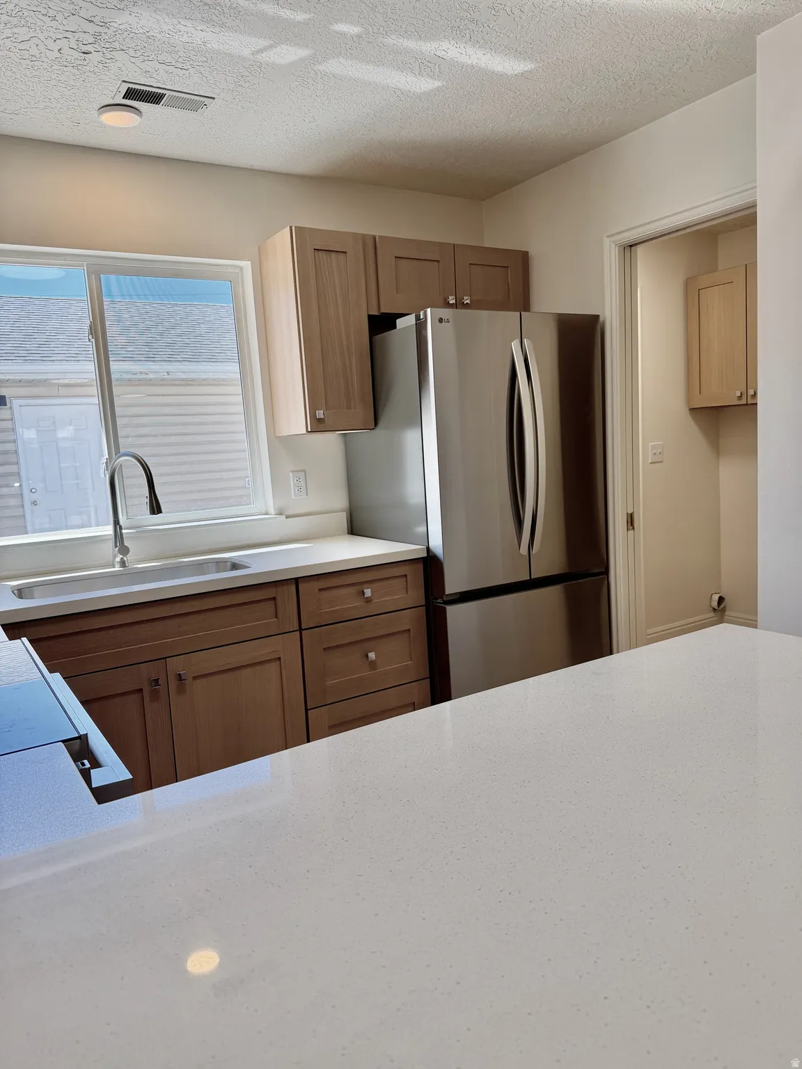 Kitchen featuring light wood-finish cabinetry, stainless steel refrigerator, white countertops, and a stainless steel sink with a gooseneck faucet