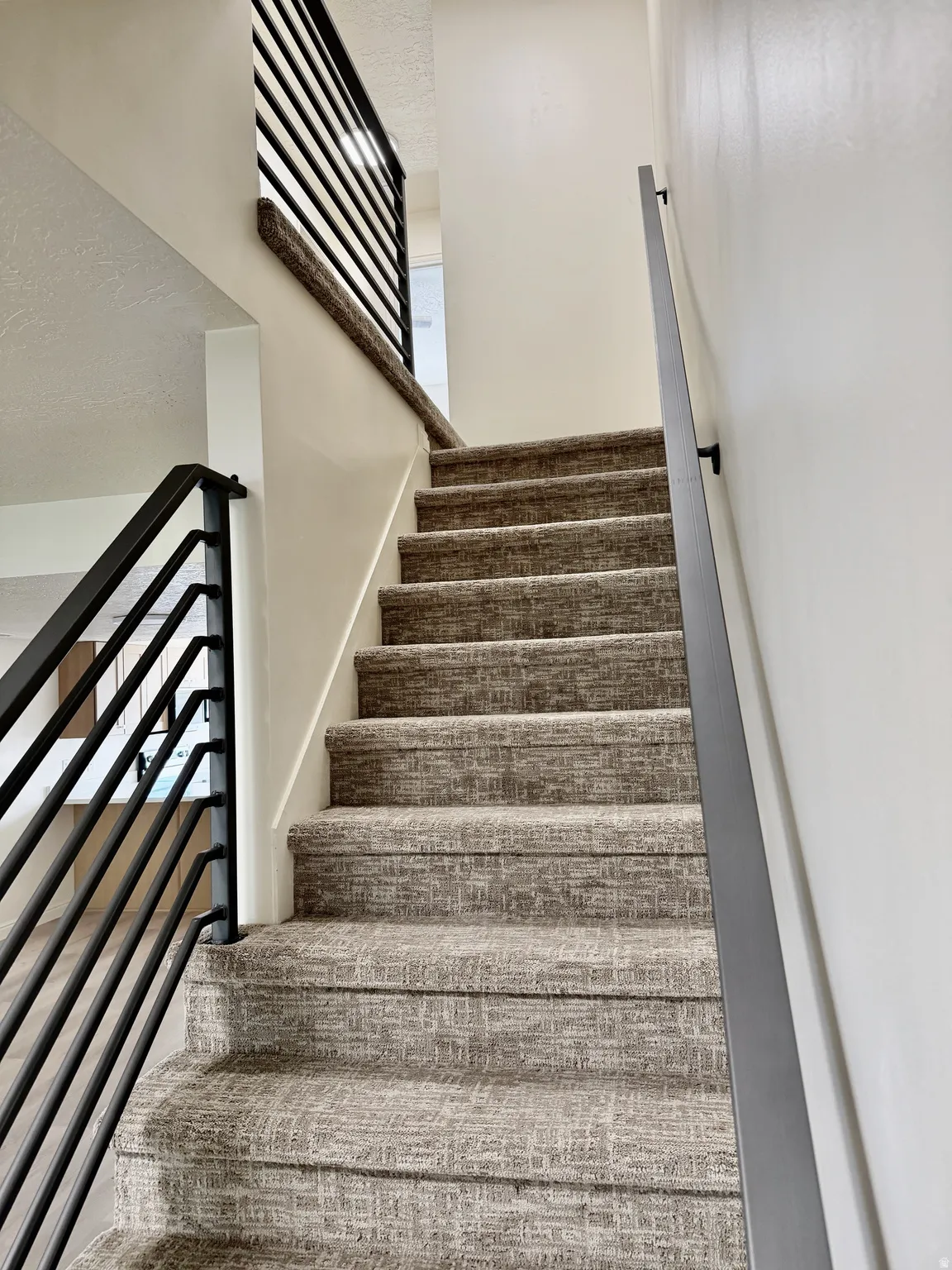 Carpeted staircase featuring a contemporary metal railing and neutral wall tones