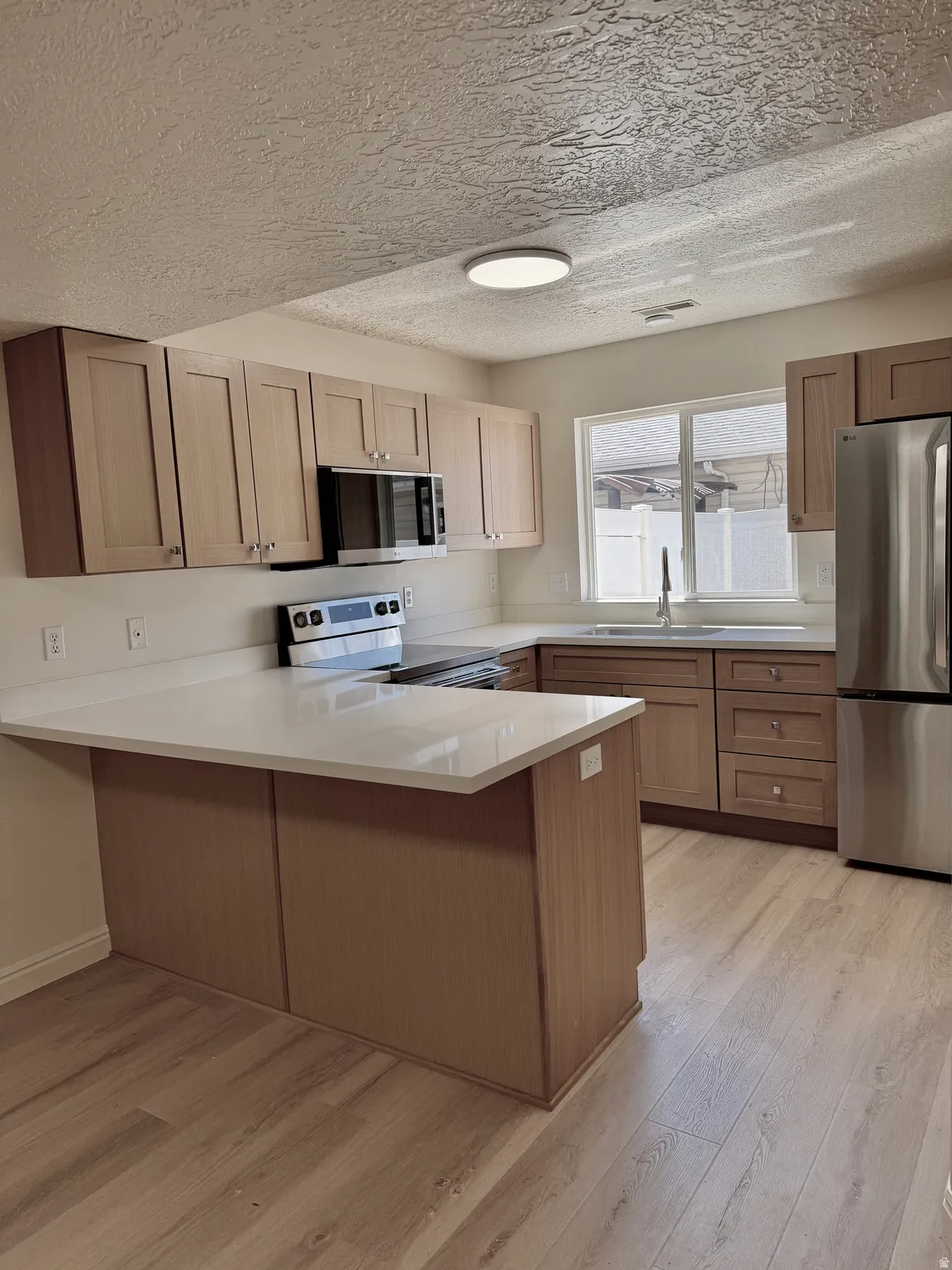 Kitchen featuring light wood-finish cabinetry, white countertops, stainless steel appliances, and wood-finish flooring
