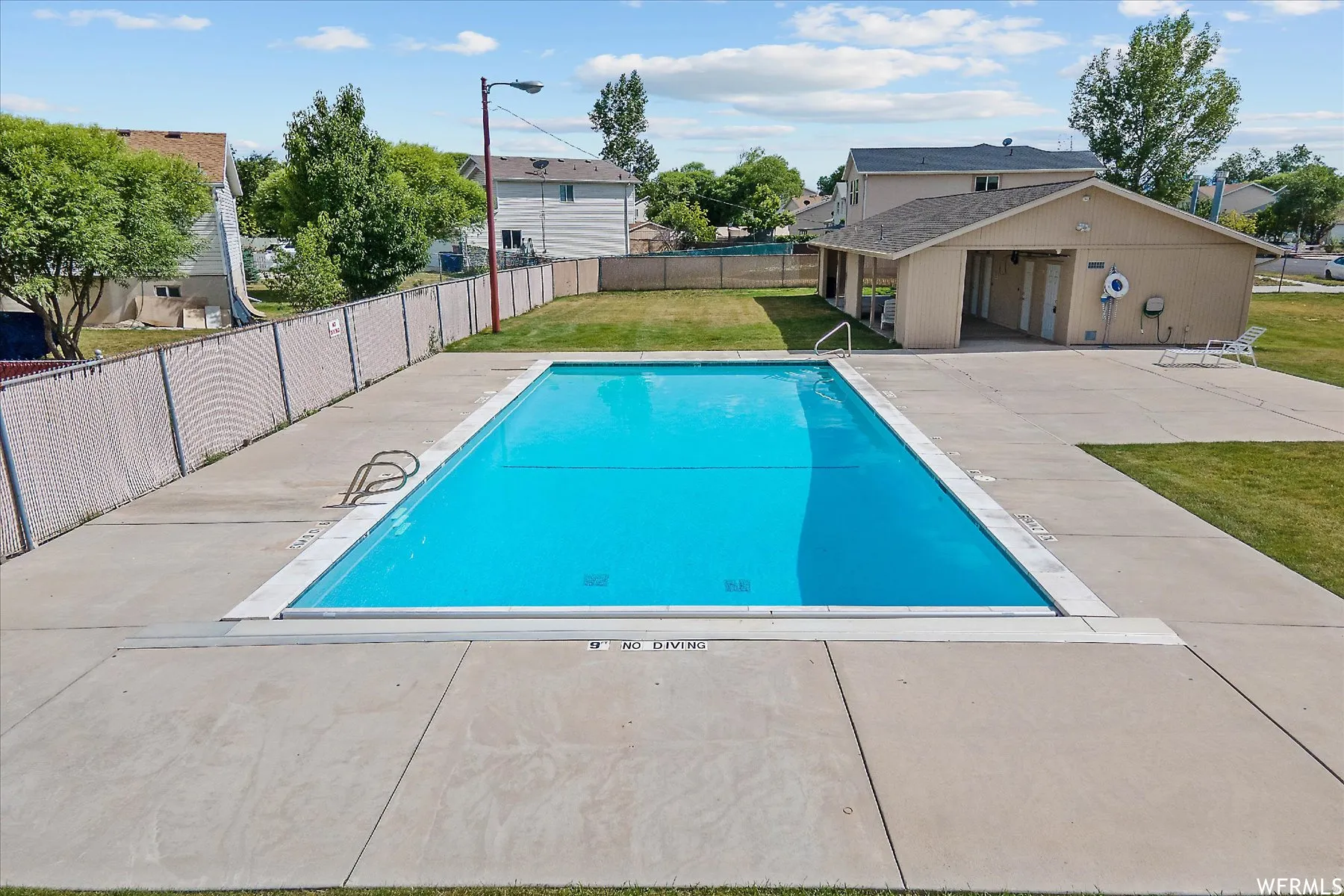 Outdoor swimming pool with concrete decking, surrounding grassy areas, and a dedicated pool house structure