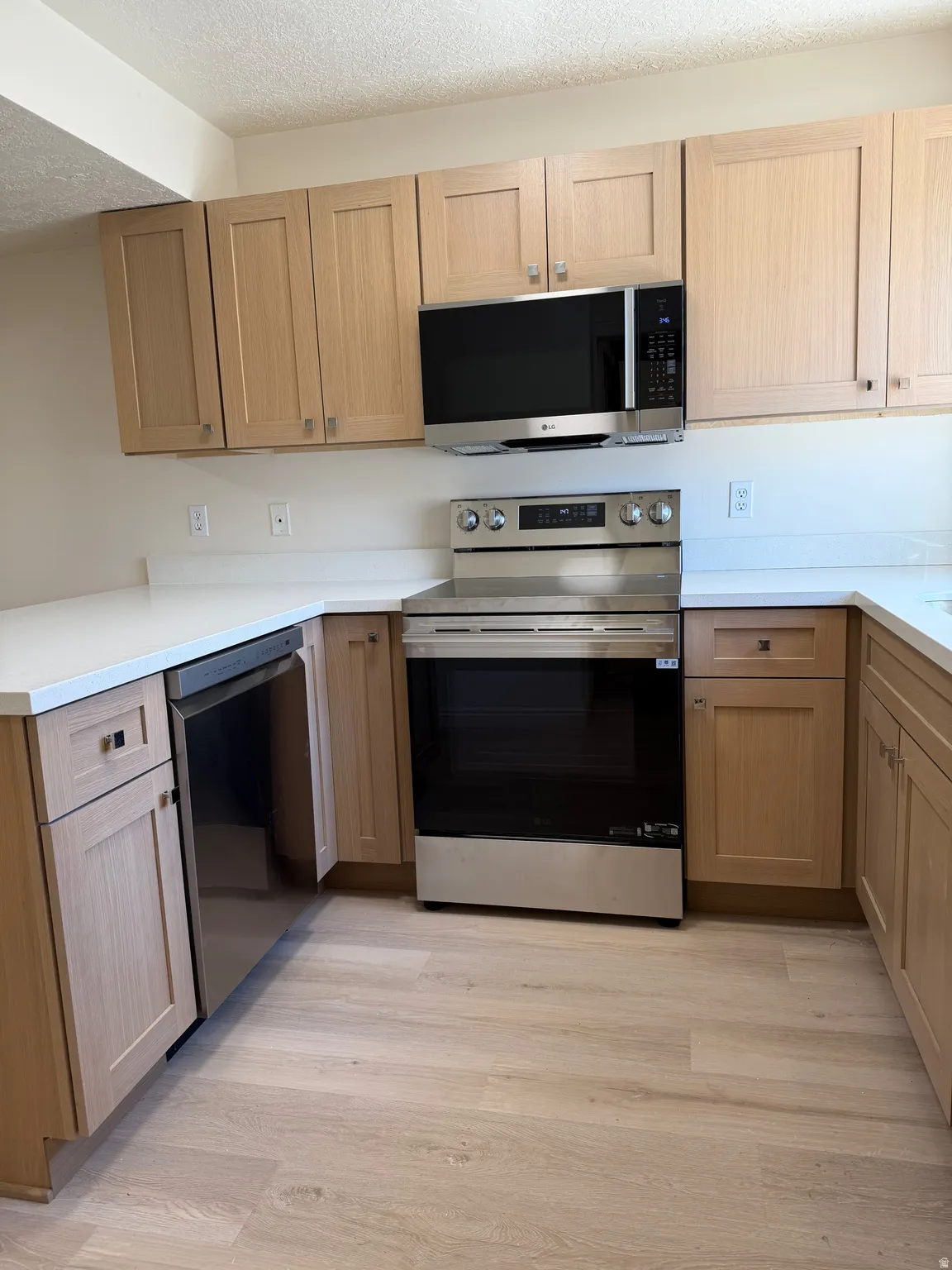 Kitchen featuring light wood-finish cabinetry, white countertops, and stainless steel appliances including a built-in microwave, range, and dishwasher