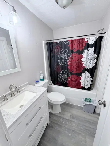 Bathroom with vanity, shower / tub combo with curtain, dark wood-style flooring, and a textured ceiling