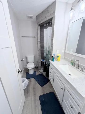 Full bath with vanity, a shower stall, a textured ceiling, and dark wood-type flooring