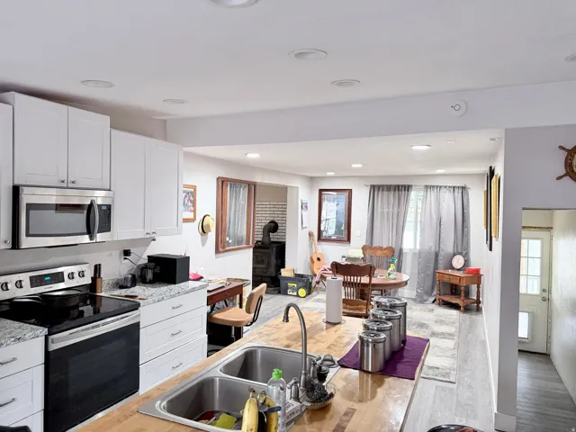 Kitchen with stainless steel appliances, white cabinetry, a wood stove, light wood-style flooring, and recessed lighting
