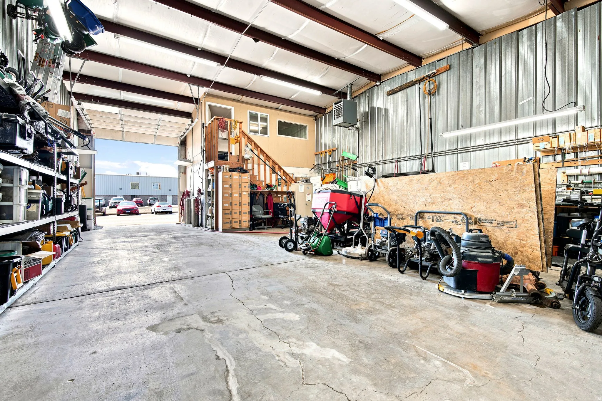 Expansive concrete floor industrial space featuring high ceilings, exposed metal beams, corrugated metal wall panels, and an interior second-level office space with a window