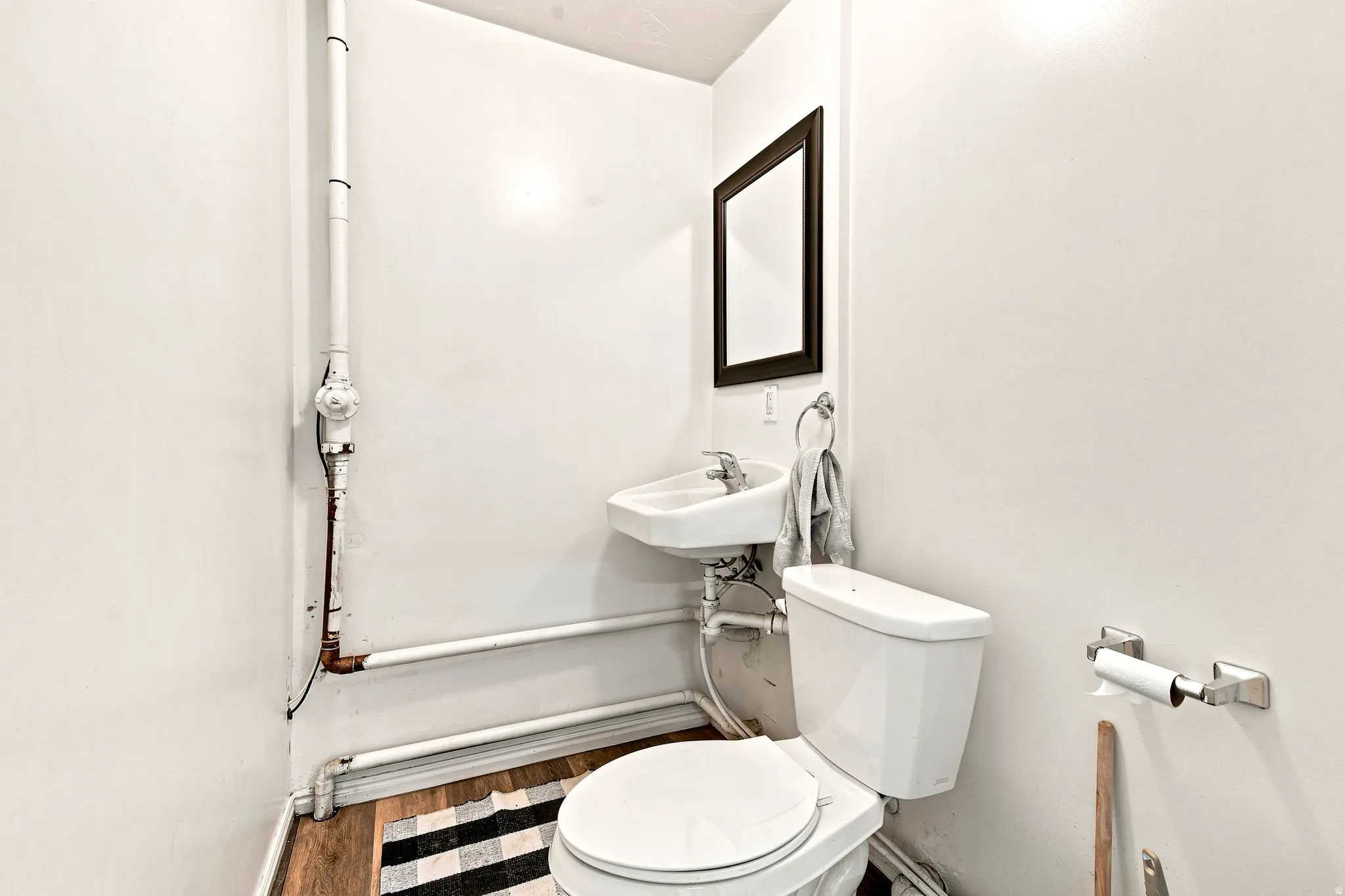 Compact bathroom featuring a wall-mounted sink with chrome faucet, a white toilet, and wood-finish flooring
