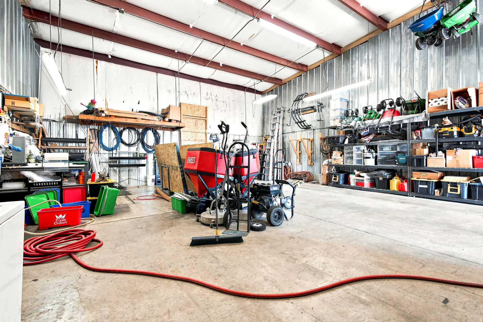 Spacious industrial-style interior featuring a concrete floor, corrugated metal walls, exposed beam ceiling, fluorescent lighting, and extensive built-in shelving