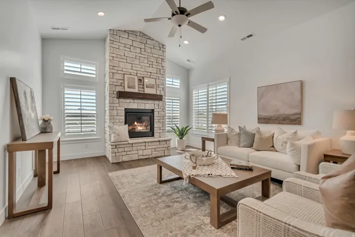 Vaulted ceiling great room featuring a floor-to-ceiling stacked stone fireplace with a wood mantel, wood-finish flooring, recessed lighting, and plantation shutters