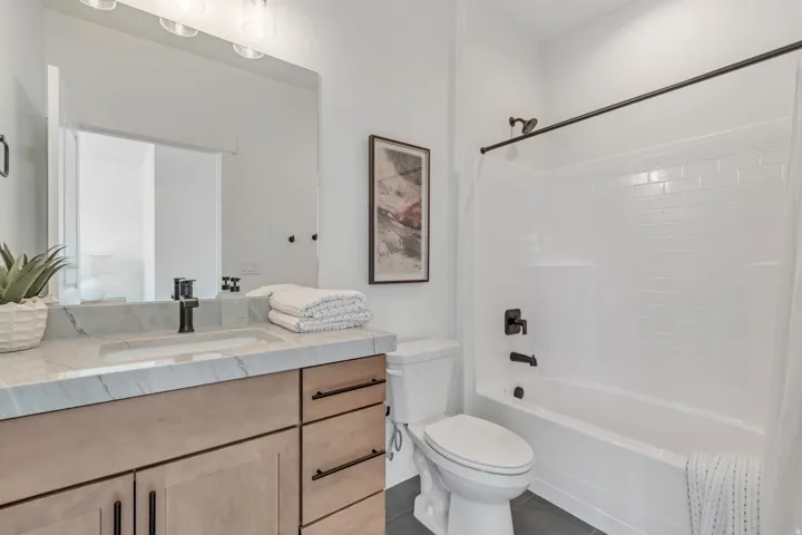 Bathroom featuring a wood-finish vanity with a light-toned countertop, an integrated sink with a matte black faucet, and a white subway tile shower surround with dark bronze fixtures