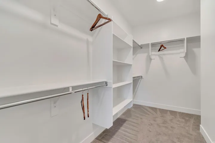 Walk-in closet featuring white built-in shelving, multiple hanging rods, recessed ceiling lighting, and grey carpeting