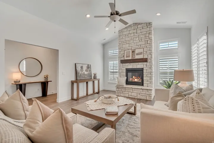 Expansive living space featuring a stone fireplace with a wood mantle, vaulted ceilings, wood-finish flooring, and white plantation shutters