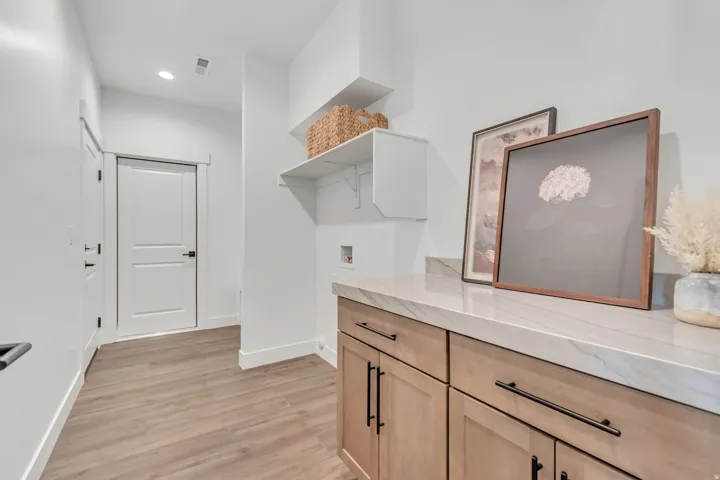 Utility room featuring wood-finish flooring, light wood cabinetry with dark hardware, and a light-toned countertop