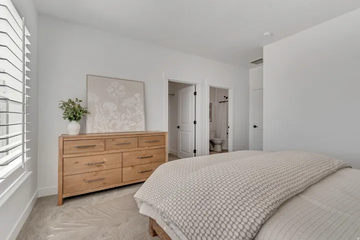 Spacious room featuring light-colored walls, carpeted flooring, and a large window with white plantation shutters
