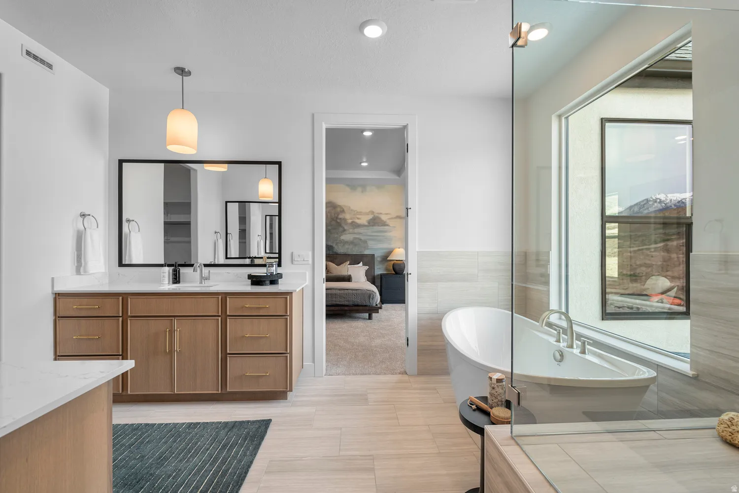 Bathroom featuring a freestanding soaking tub, large window, glass-enclosed shower, double vanity with light wood cabinetry, and light wood-finish flooring