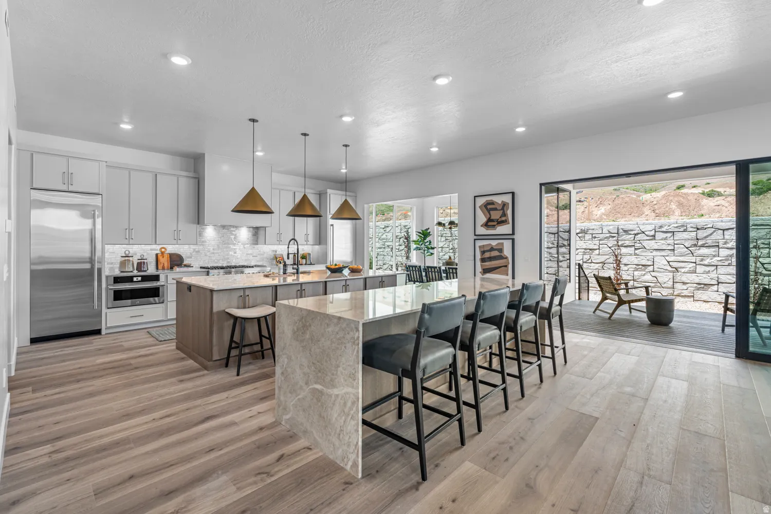 Gourmet kitchen featuring a waterfall island with seating, pendant lighting, stainless steel appliances, and light wood-finish flooring