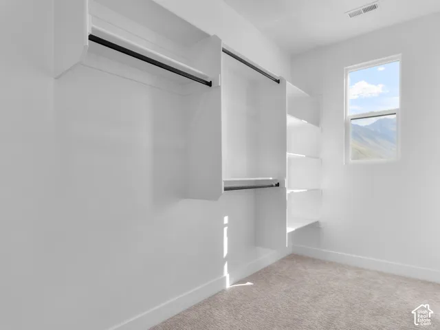 Walk-in closet featuring white built-in shelving, tiered hanging rods, carpeted flooring, and a window framing mountain scenery