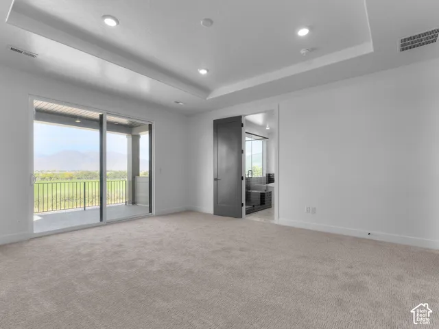 Tray ceiling with recessed lighting, wall-to-wall carpeting, sliding glass doors to a covered balcony, and a mountain landscape backdrop