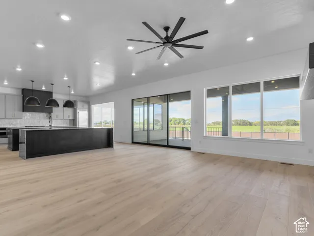 Open-concept living space featuring wood-finish flooring, a large kitchen island, recessed lighting, a modern ceiling fan, and expansive windows