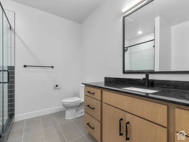 Bathroom featuring a wood-finish vanity with a dark stone countertop, an integrated rectangular sink, matte black hardware, and a glass-enclosed shower with tile surround