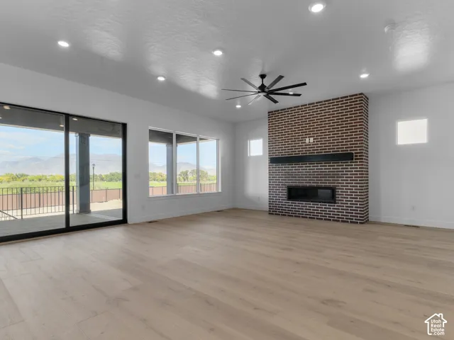 Open-concept living space featuring wood-finish flooring, a full-height brick fireplace, recessed lighting, a modern ceiling fan, and sliding glass doors with mountain scenery