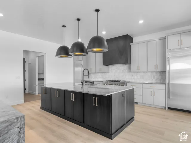 Kitchen featuring a central island with dark cabinetry, light-toned stone countertops, three matte black dome pendant lights, white shaker-style perimeter cabinetry, and a custom dark wood-finish range hood