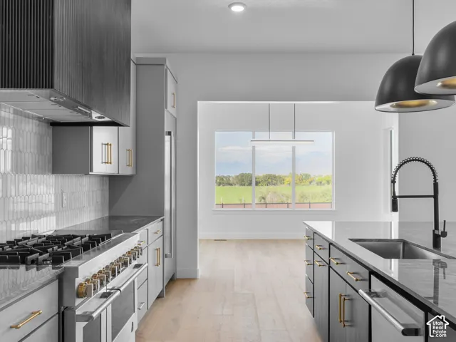 Kitchen featuring a professional-grade range, custom cabinetry with metallic hardware, stone countertops, integrated backsplash, and wood-finish flooring