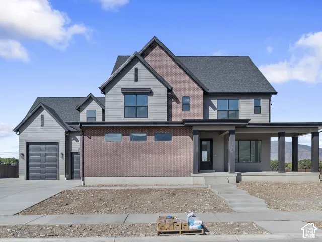 Two-story exterior featuring a mix of red brick and horizontal siding, multiple gables, a covered front porch with square columns, and a multi-car garage