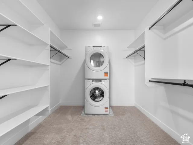 Walk-in closet featuring floor-to-ceiling custom shelving, dual-level hanging rods, wall-to-wall carpeting, and a stacked laundry unit