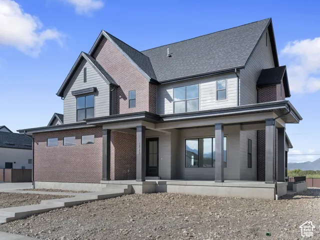 Two-story exterior featuring multi-gabled rooflines, a blend of brick and horizontal siding, a covered front porch with square columns, and expansive windows