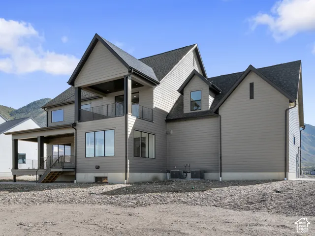 Multi-level exterior featuring horizontal siding, a covered balcony with metal railing, a covered ground-level patio, and mountain backdrop