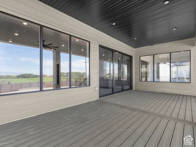 Covered deck featuring composite decking, recessed ceiling lighting, a dark-toned beadboard ceiling, large-format glass sliding doors, and expansive floor-to-ceiling windows
