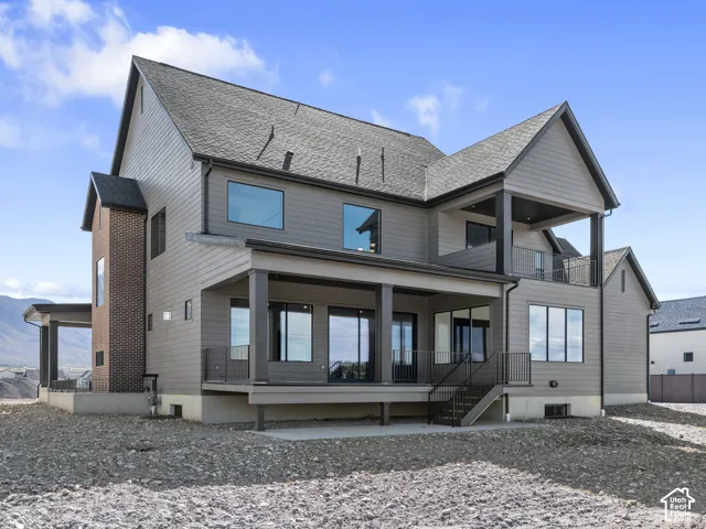 Multi-story exterior featuring horizontal siding, brick masonry detailing, a covered ground-level patio, an upper-level balcony, and expansive window placements