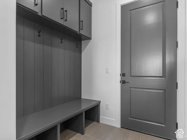 Built-in gray cabinetry with vertical shiplap detailing, overhead storage, integrated bench seating, and matte black hardware, featuring a matching gray solid-core door and wood-finish flooring