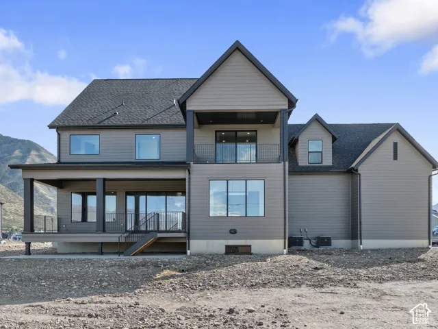 Two-story exterior featuring horizontal siding, a covered patio with metal railing, a second-story balcony, and large-format windows set against a mountainous backdrop