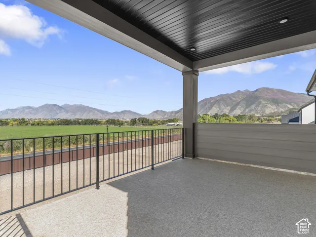 Covered balcony with a dark wood-finish ceiling, mountain backdrop, iron railing, and concrete flooring