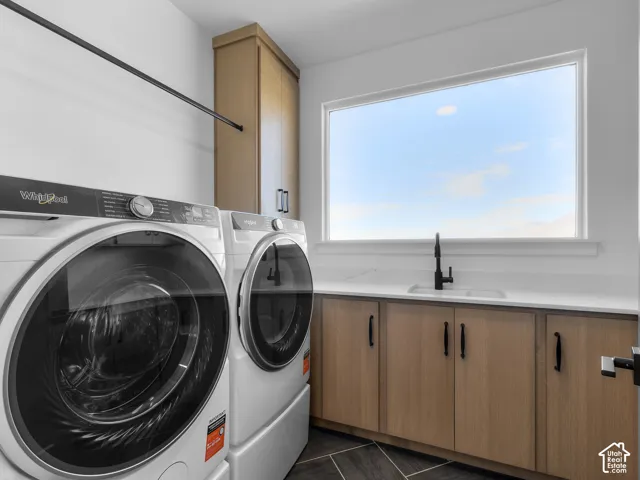 Laundry room featuring wood-finish cabinetry, white solid-surface countertops, an undermount sink with a matte black faucet, and herringbone-patterned flooring