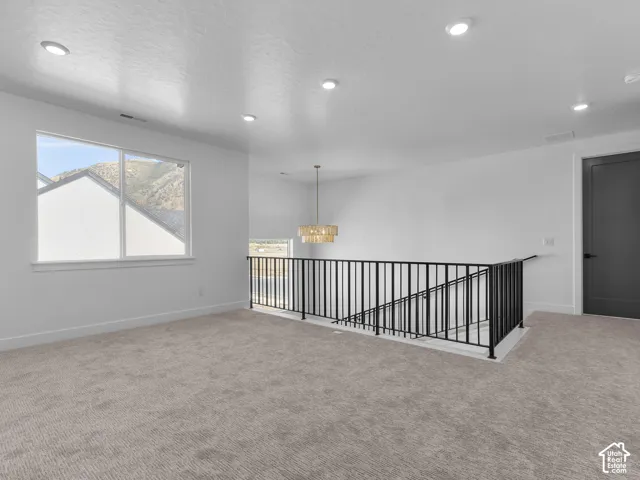 Open floor plan featuring recessed lighting, a tiered chandelier, black metal railing, and wall-to-wall carpeting