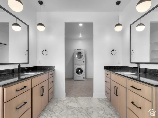 Dual vanities featuring light wood-finish cabinetry, dark stone countertops, framed mirrors, and matte black pendant lighting, paired with stone tile flooring