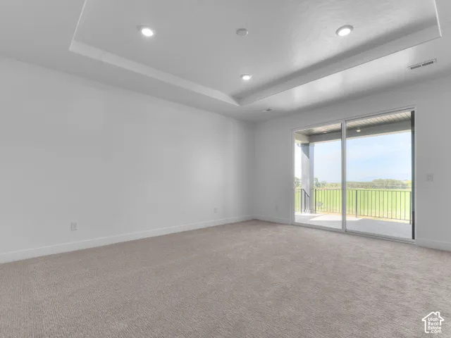 Tray ceiling with recessed lighting, neutral carpeting, and a sliding glass door providing exterior access to a covered balcony