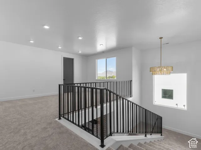 Open area featuring neutral wall-to-wall carpeting, recessed ceiling lighting, a tiered drum pendant fixture, and a black metal railing
