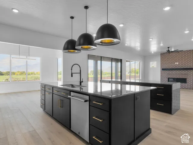 Kitchen island featuring stone countertops, matte black cabinetry, and gold-finish hardware, illuminated by three pendant lights, with wood-finish flooring and a brick fireplace