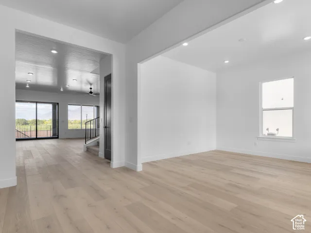 Open-concept interior featuring light wood-finish flooring, recessed lighting, expansive glass sliding doors, and a dark-toned interior door