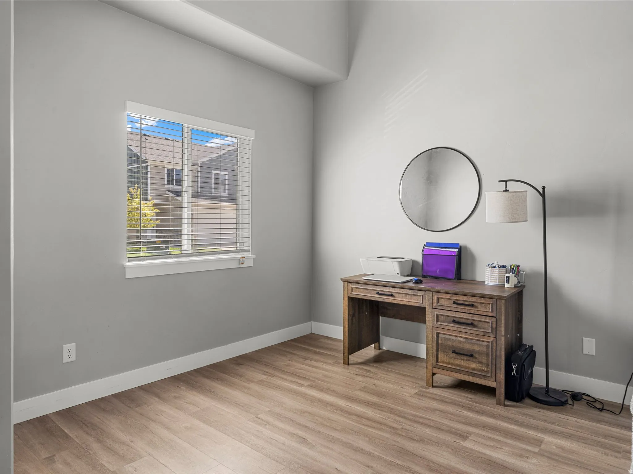 Bright room featuring wood-finish flooring, a window with white blinds, and light gray walls