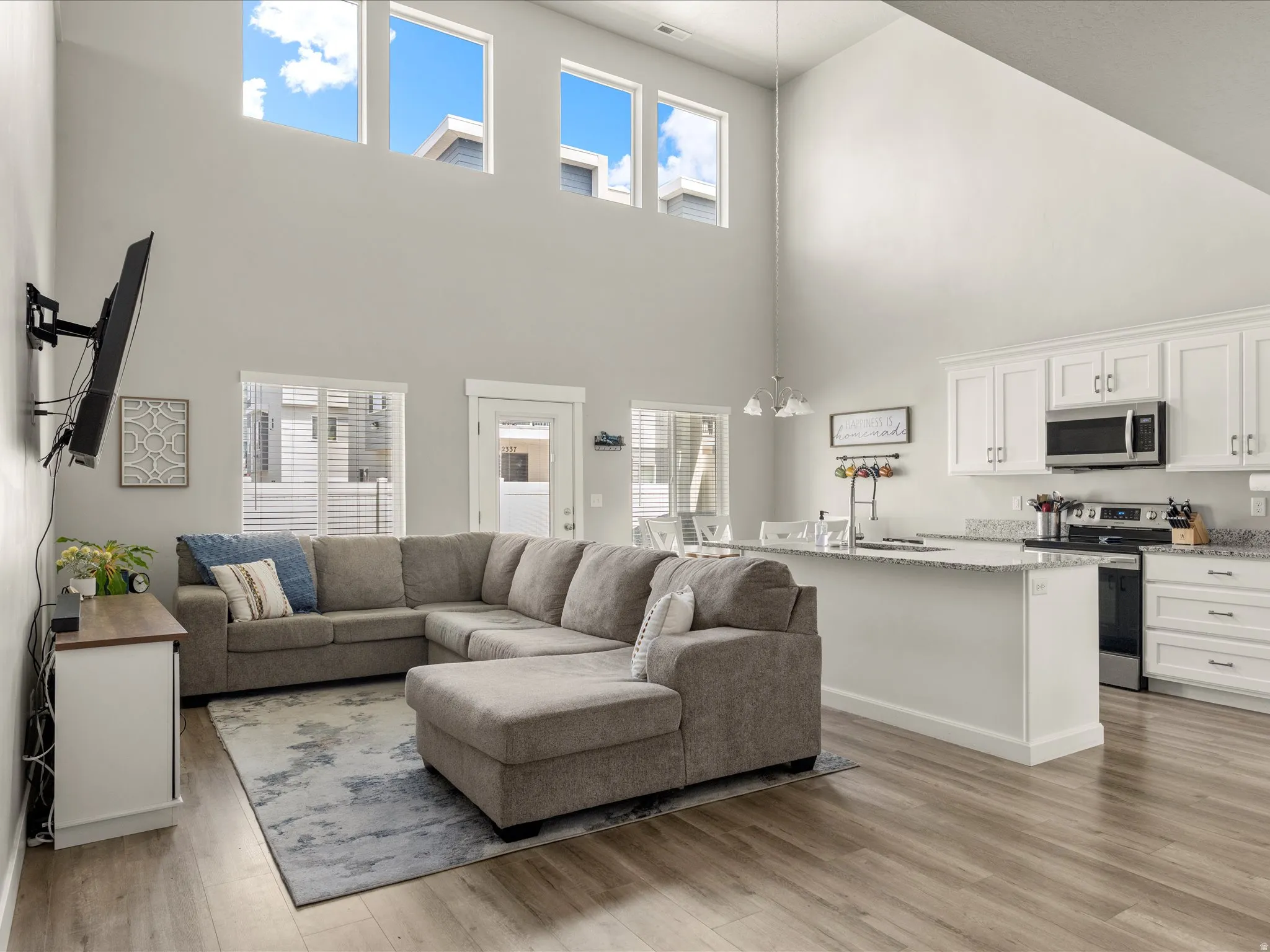 Vaulted ceilings with high transom windows, an open-concept layout, wood-finish flooring, white shaker cabinetry, and granite-style countertops