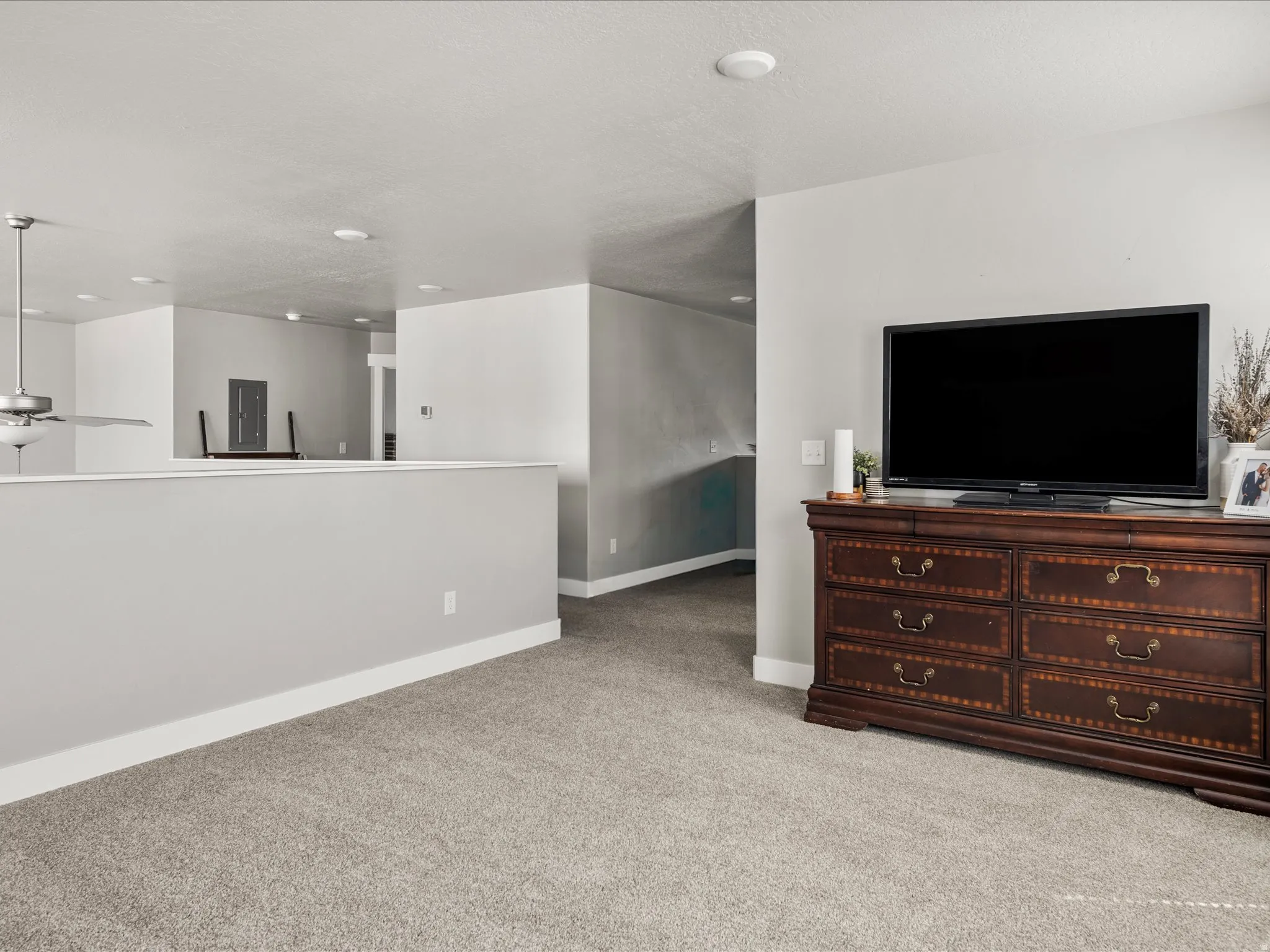 Carpeted interior space featuring a partial-height wall, a ceiling fan with integrated lighting, recessed lighting, and white baseboards