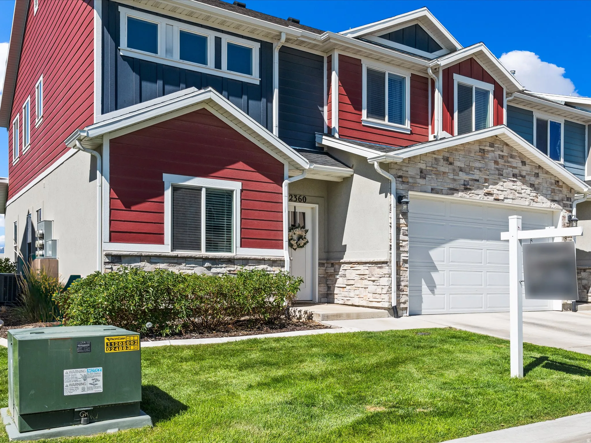 Multi-level townhouse exterior featuring red and dark blue siding, stone veneer accents, an attached garage, and a manicured lawn