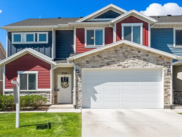Multi-story residence featuring a two-car garage with overhead door, stone veneer accents, contrasting red and blue siding, and a covered entry with an opaque front door